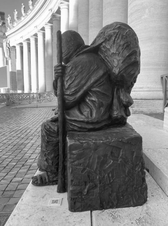 Schwarz-weiße Aufnahme einer gebeugten Figur mit Wanderstab vor einer Säulenhalle.